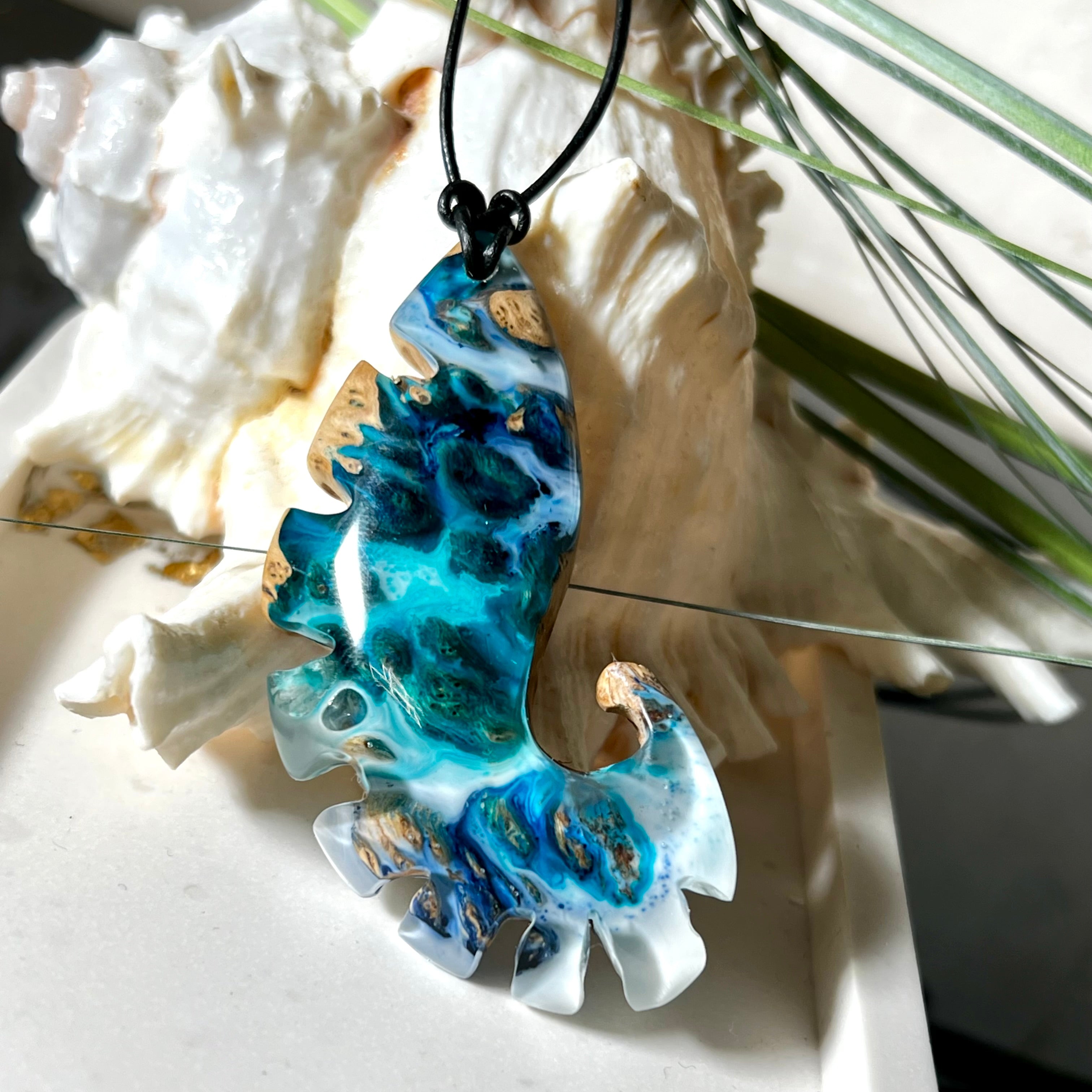 Ocean Nautilus Halskette – handgefertigter Anhänger aus  Epoxidharz und edlem Maserholz in kräftigem Blau, Türkis und Weiß, geformt wie eine stilisierte Nautilus-Muschel. Die einzigartige Maserung des Holzes trifft auf transparente Tiefenwirkung des Harzes. Der ca. 7 cm große Anhänger hängt an einem verstellbaren Lederband mit dekorativen Holzperlen (26–48 cm). Jedes Stück ist ein maritimes Unikat, inspiriert von der Magie des Meeres.