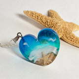 Ein herzförmiger Anhänger mit einer ganzen Ozeanwelt darin: Welle, Sand und Seestern in leuchtendem Blau und Türkis – handgegossen, einzigartig, unvergesslich. Mit versilberter Kette (46 cm) und Edelstahl-Karabiner.