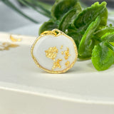 Gold-colored pendant with gold flakes, background in white and fluorescent under black light, birthday, gift