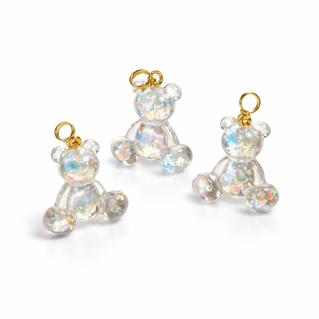 Kleiner Bärchen-Anhänger aus transparentem Harz mit irisierenden Flakes in Regenbogen-Schimmer, goldfarbene Anhängerschlaufe aus Edelstahl. Größe ca. 2,2 × 2,1 cm. Handgefertigtes Unikat; Flakes-Anordnung variiert, vereinzelt kleine Luftbläschen möglich.