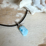 Larimar Freeform Anhänger mit rhodinierter Silberöse an schwarzer Lederkette. Der seltene, kostbare Larimar („Atlantisstein“) zeigt ein lebendiges Muster aus Türkis- und Weißtönen. Beidseitig tragbar, Steingröße ca. 2 x 1 cm, Lederkette 45 cm mit Edelstahl-Karabiner und 5 cm Verlängerung. Natürlicher, maritimer Unikatschmuck.