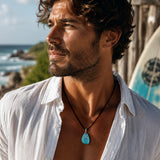 KI-Tragebild MEERESTROPFEN – handgefertigte Seeglas Halskette mit türkisblauem Tropfen-Anhänger, Walflossen-Charm aus Edelstahl und schwarzer Lederschnur, maritimer Unisex Schmuck für Männer im Surf- und Strandlook.
