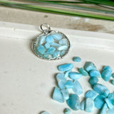 Runder Anhänger „Atlantis Dream“ aus antik-silberfarbener Zinklegierung, gefüllt mit kleinen Larimar-Edelsteinchen und klarem Resin. Die Larimarsteine zeigen sanfte Blau- und Weißtöne, die an das Meer erinnern. Durchmesser ca. 22 mm, handgefertigtes Unikat, fotografiert auf maritimem Untergrund mit kleinen Larimarsteinen und Muscheln zur Größenorientierung.