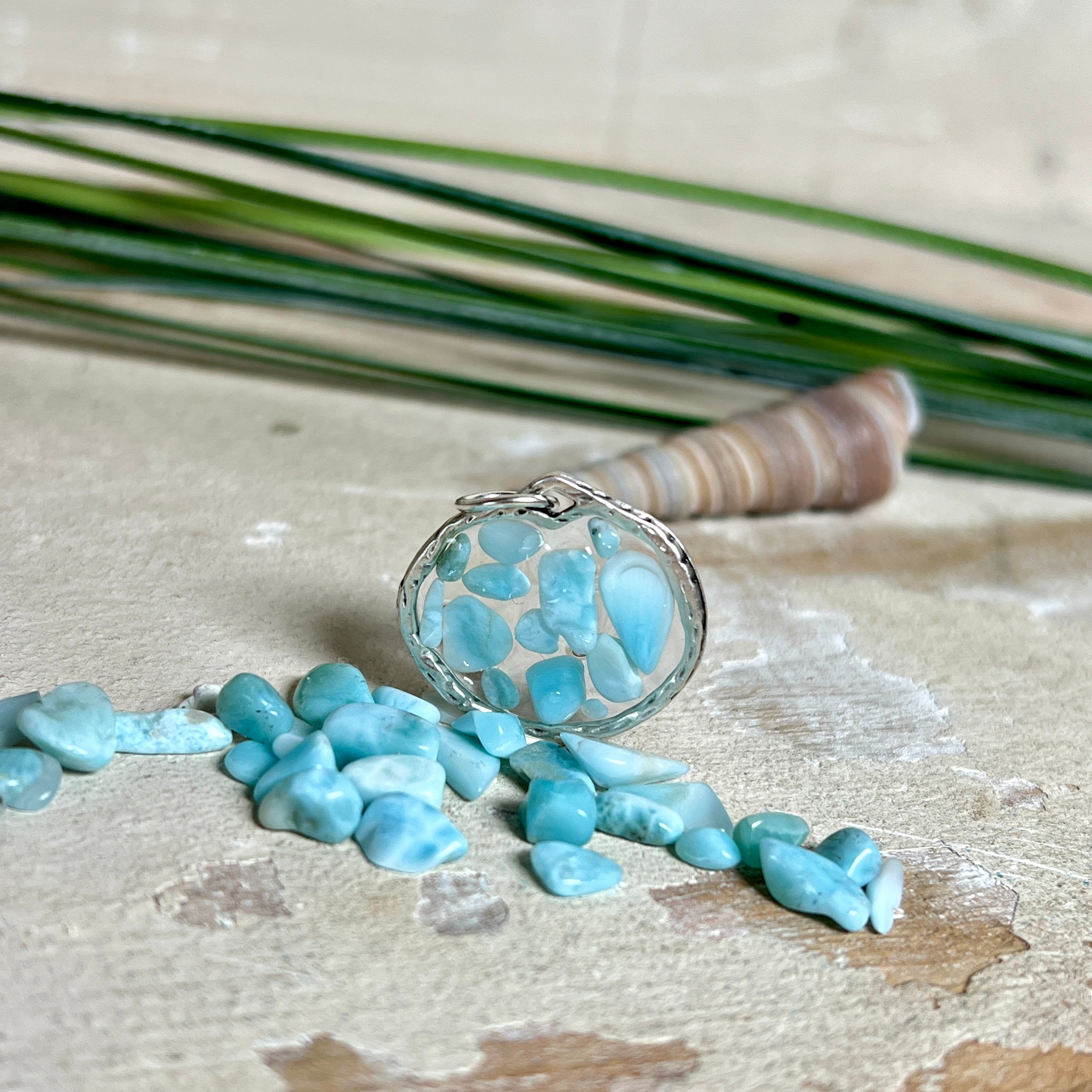 Runder Anhänger „Atlantis Dream“ aus antik-silberfarbener Zinklegierung, gefüllt mit kleinen Larimar-Edelsteinchen und klarem Resin. Die Larimarsteine zeigen sanfte Blau- und Weißtöne, die an das Meer erinnern. Durchmesser ca. 22 mm, handgefertigtes Unikat, fotografiert auf maritimem Untergrund mit kleinen Larimarsteinen und Muscheln zur Größenorientierung.