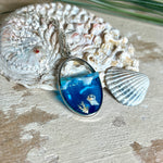 „Riffschatz“ – ovaler Harz-Anhänger mit plastischer 3D-Welle in Blau/Türkis, weißer Schaumkrone und Muschel-/Korallen-Stickern am Grund. Die Sticker sind unter klarem Harz versiegelt. Silber-Legierung, ca. 3,9 × 2,3 cm, an einer ca. 56 cm langen versilberten Kette. Handgefertigt, hochglänzend, jedes Stück ein Unikat.