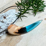 Handgefertigter Anhänger aus Edelholz und transparent-türkisblauem Epoxidharz, glatt poliert. Größe ca. 6,7 × 2,0 cm. Mit Edelstahlöse an schwarzer Lederkette (45 cm + 5 cm Edelstahl-Verlängerung, Karabiner). Maritimer, moderner Unisex-Schmuck mit natürlicher Holzmaserung; kleine Lufteinschlüsse sind charakteristisch.
