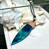 Beidseitig tragbarer Surfbrett-Anhänger aus Olivenholz, kombiniert mit klaren Epoxidharz in Blau-Grün. Eingearbeiteter synthetischer Opal erzeugt ein faszinierendes Farbspiel wie Nordlichter. Größe ca. 6 × 1,8 cm. Mit verstellbarem Lederband (26–45 cm), dekorativen Perlen & Schiebeknoten. Handgefertigt & einzigartig. Ein Schmuckstück mit Naturinspiration.