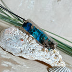 Rechteckiger Stabanhänger aus Maserholz und glasklarem Epoxidharz in tiefen Blau- und Türkistönen mit organischer Lagunen/Riff-Optik. Hochglanzpoliert, ca. 4,6 × 1,2 cm. Der Anhänger hängt an einer schwarzen Lederkette mit Edelstahl-Karabiner und 5-cm-Verlängerung (45 + 5 cm); die Anhängerschlaufe ist ebenfalls aus Edelstahl. Handgefertigtes Unikat, Lieferung in edler Schmuckbox – maritimer Look.