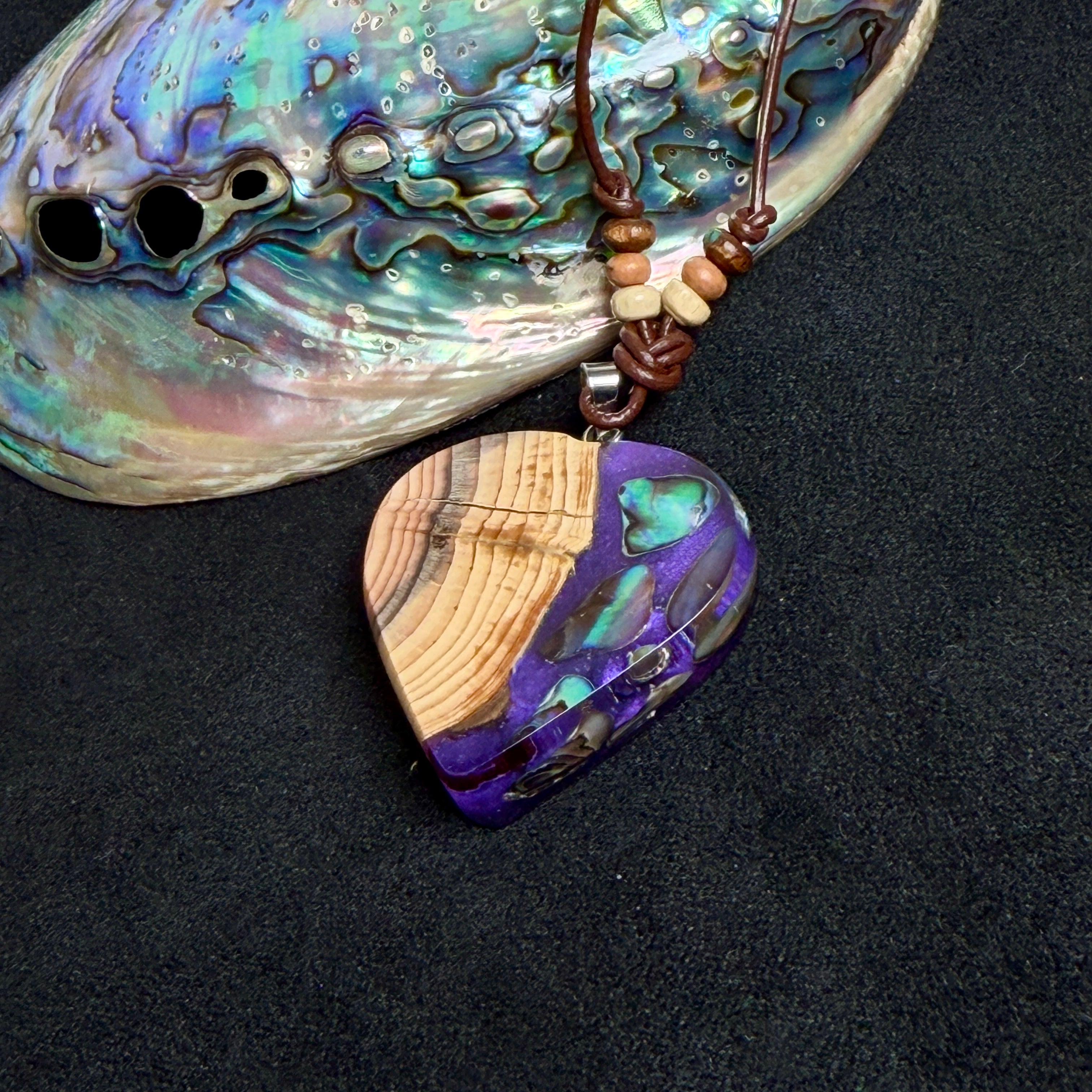 Handgemachter Herzanhänger aus Eibenholz mit lila Harz und Paua-Muschel-Inlay an braunem, verstellbarem Lederband.