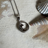 Feine Wellen-Kette aus rhodiniertem 925 Silber. Der runde Anhänger zeigt eine stilisierte Welle mit hellblauem Larimar-Cabochon, eingefasst in poliertem Silber. Größe des Anhängers ca. 23 x 13 mm, an einer 45 cm langen, 1 mm starken, rhodinierten Silberkette. 