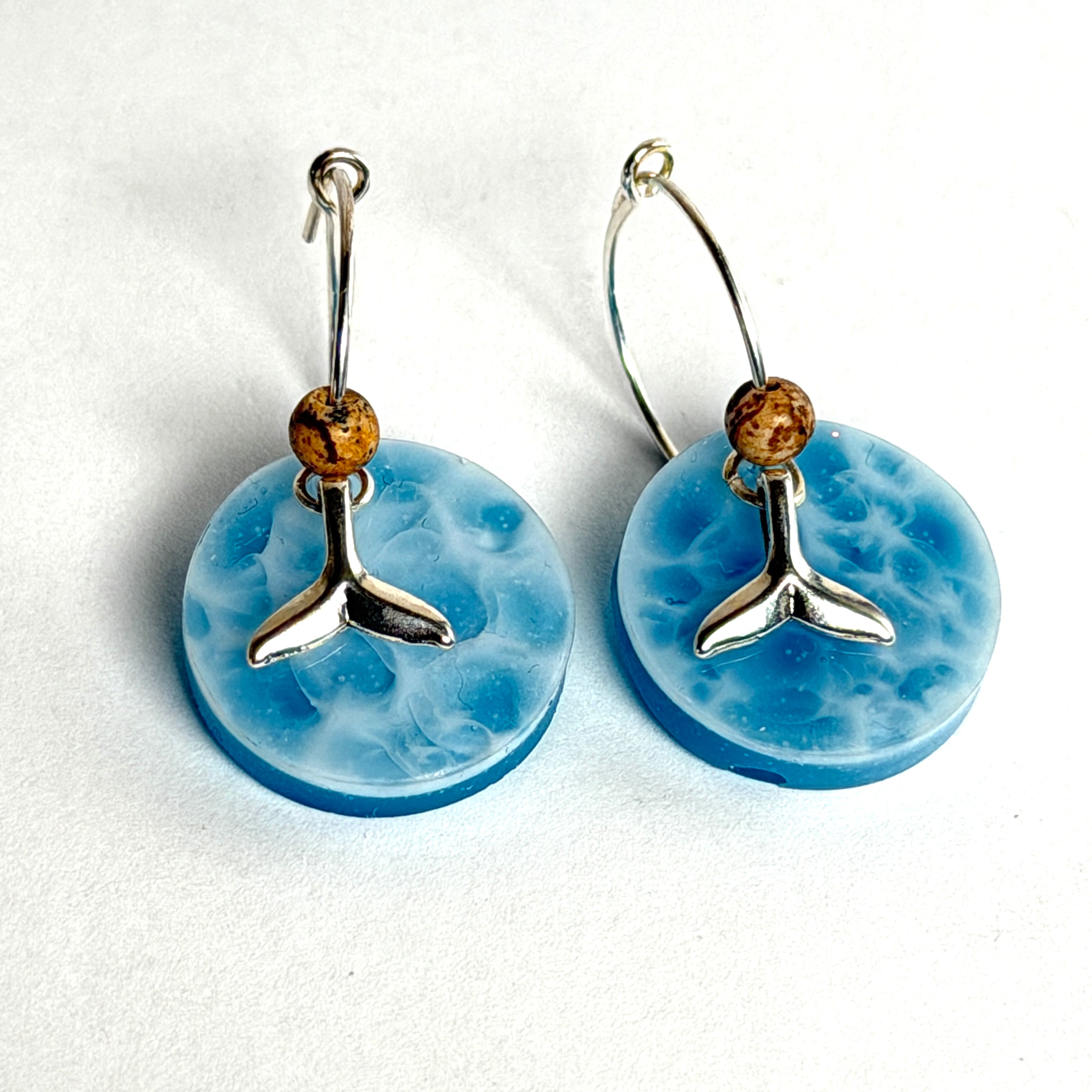 Handgefertigte Creolen-Ohrringe mit hellblauer Resin-Scheibe, zarter Wolkenmarmorierung, silbernem Walflosse-Charm und Jaspis-Natursteinperle. 925 Silber Creole, Gesamtlänge ca. 3,5 cm – Ocean-Feeling für jeden Tag.