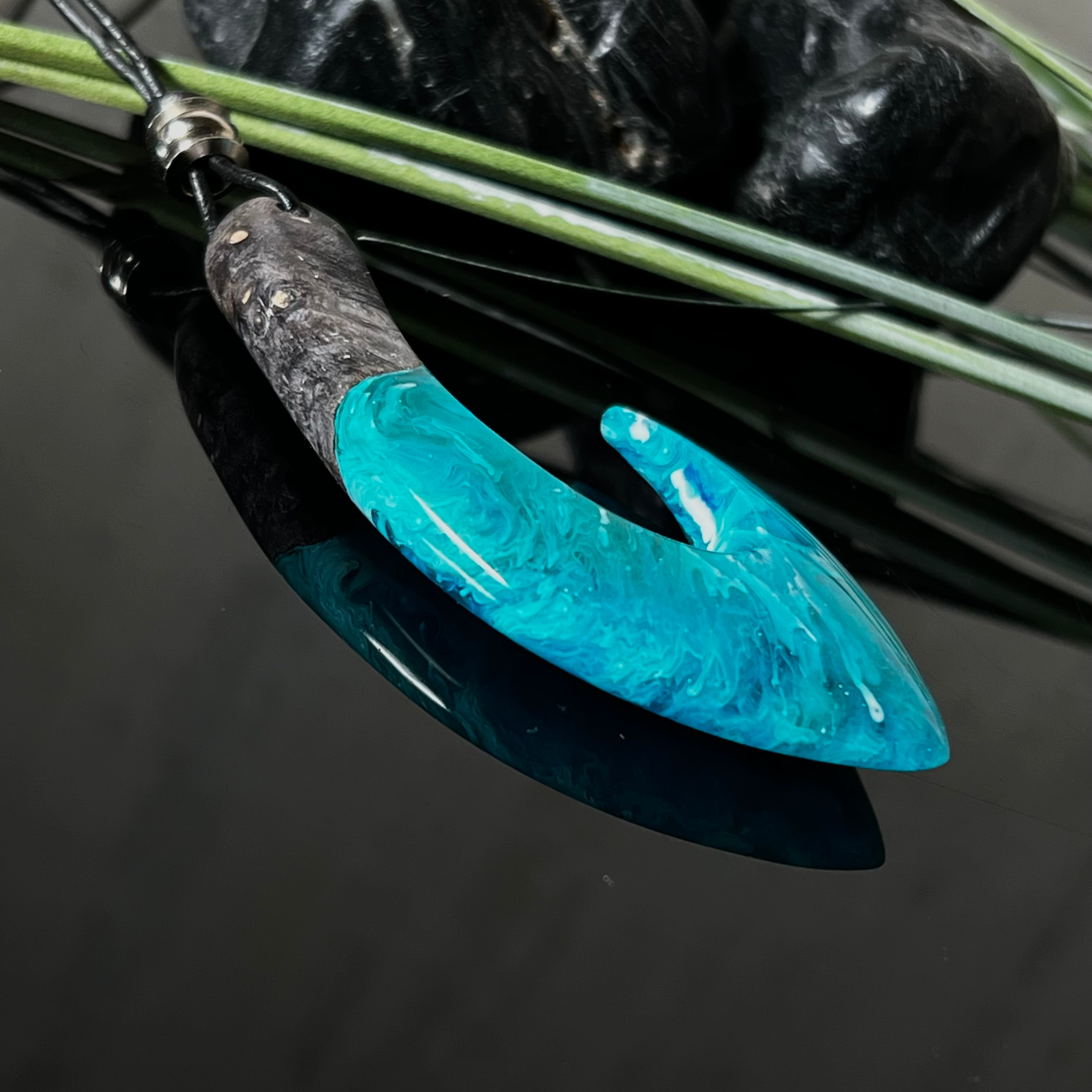 Handgefertigter Maori-Anhänger „Tangaroa Spirit“ in traditioneller Hakenform, gefertigt aus stabilisiertem Maserholz und ozeanblauem Harz. Die polierte Oberfläche bringt die natürlichen Maserungen und das tiefblaue Farbspiel besonders zur Geltung. Symbolisiert Schutz, Stärke und die Verbundenheit zum Meer. Verstellbares Lederband mit Schiebeknoten und dekorativen Holz- sowie Metallperlen – ideal als kraftvoller Talisman oder Geschenk.