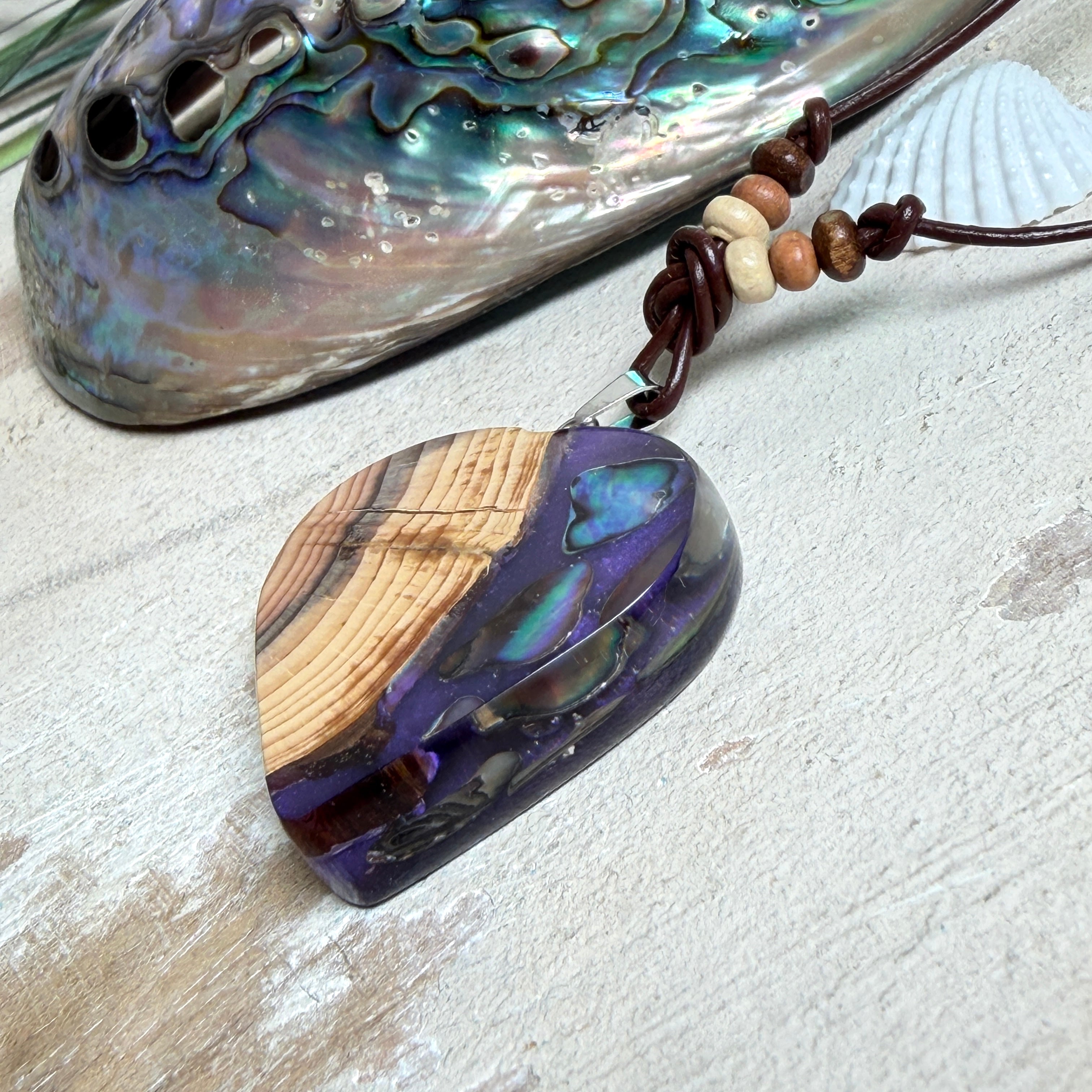 Handgemachter Herzanhänger aus Eibenholz mit lila Harz und Paua-Muschel-Inlay an braunem, verstellbarem Lederband.