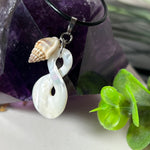 Detailaufnahme eines handgefertigten Anhängers aus echtem Perlmutt in Schlaufenform, kombiniert mit einer kleinen echten Muschel als Charm-Anhänger. Der Schmuck hängt an einer feinen schwarzen Lederschnur mit Edelstahlverschluss und symbolisiert Harmonie und Unendlichkeit. Ideal für Meeresliebhaberinnen und Fans von Naturmaterialien.