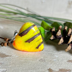 Herz-Anhänger aus Pinienzapfen & Harz, fluoreszierend bei Schwarzlicht. Farben Gelb-Orange-Weiß, Größe 4,2 × 3,8 cm. Lederband verstellbar.