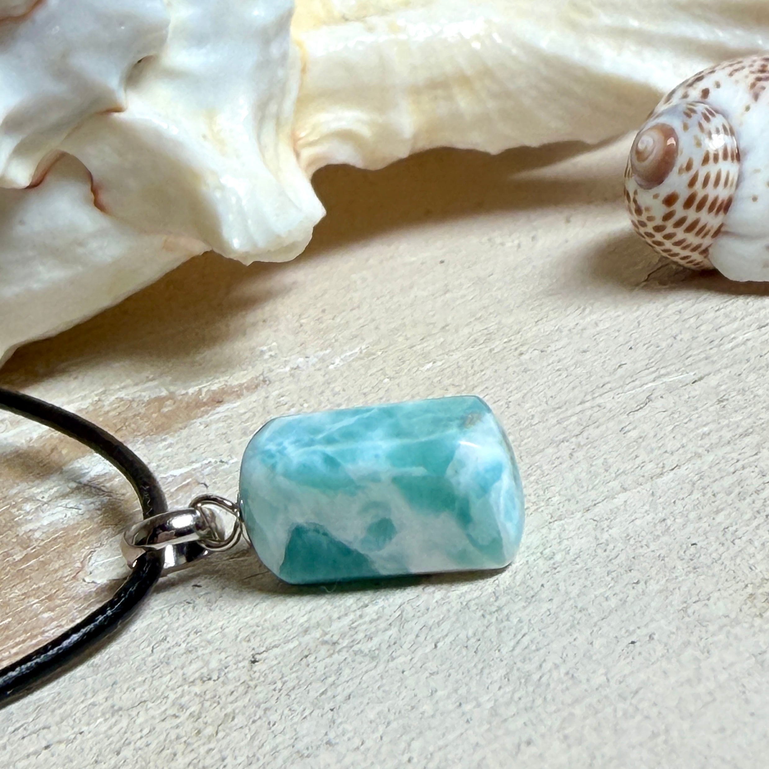 Larimar Freeform Anhänger an schwarzer Lederkette. Natürlicher, rechteckiger Larimar-Stein (ca. 1,5 × 1 cm) in Türkis-Blau mit weißen Strukturen, eingefasst in eine rhodinierte Silberöse. Beidseitig tragbar, an 45 cm Lederkette mit Edelstahl-Karabinerverschluss und 5 cm Verlängerung. Maritimes, zurückhaltend elegantes Schmuckstück mit der Optik karibischen Meerwassers.
