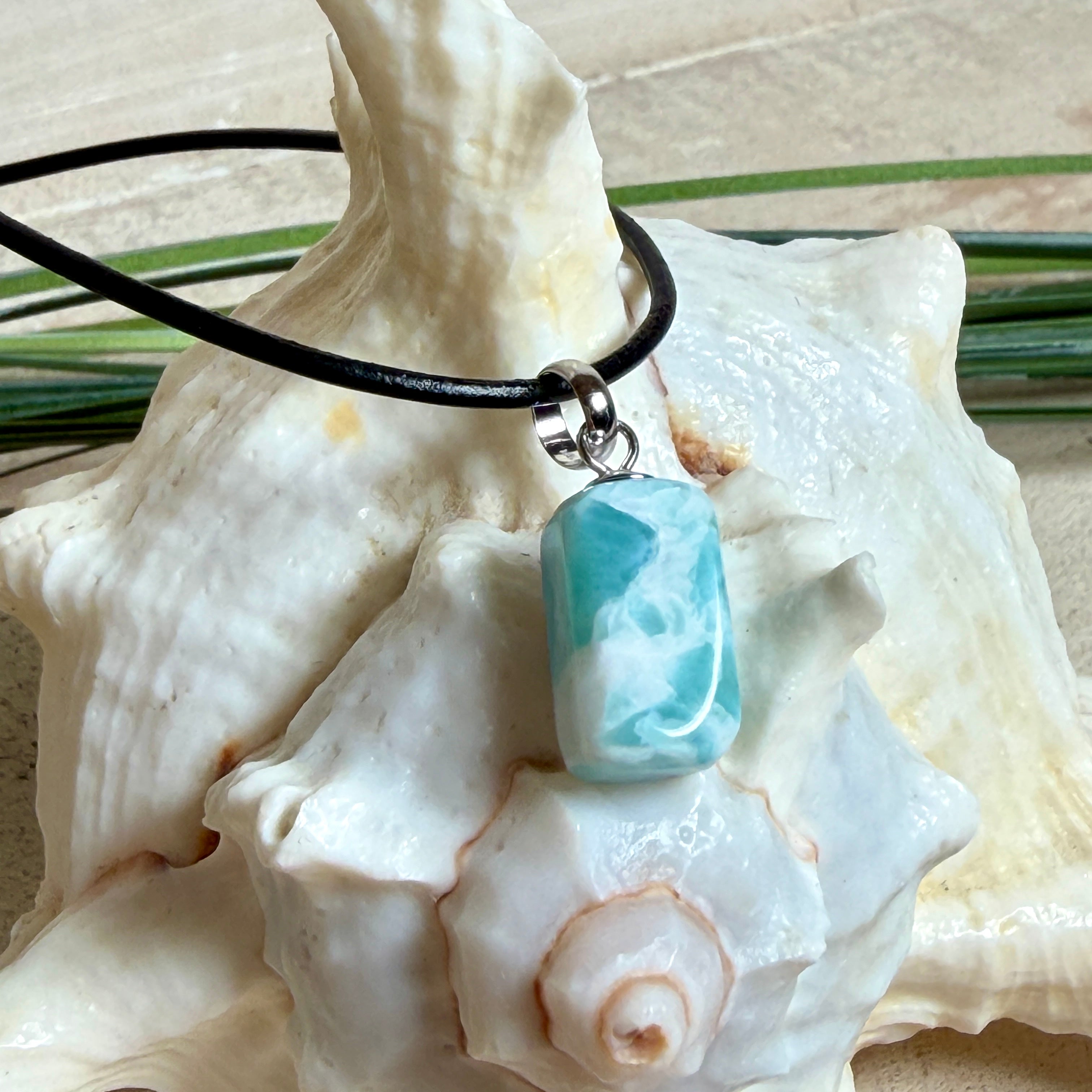 Larimar Freeform Anhänger an schwarzer Lederkette. Natürlicher, rechteckiger Larimar-Stein (ca. 1,5 × 1 cm) in Türkis-Blau mit weißen Strukturen, eingefasst in eine rhodinierte Silberöse. Beidseitig tragbar, an 45 cm Lederkette mit Edelstahl-Karabinerverschluss und 5 cm Verlängerung. Maritimes, zurückhaltend elegantes Schmuckstück mit der Optik karibischen Meerwassers.