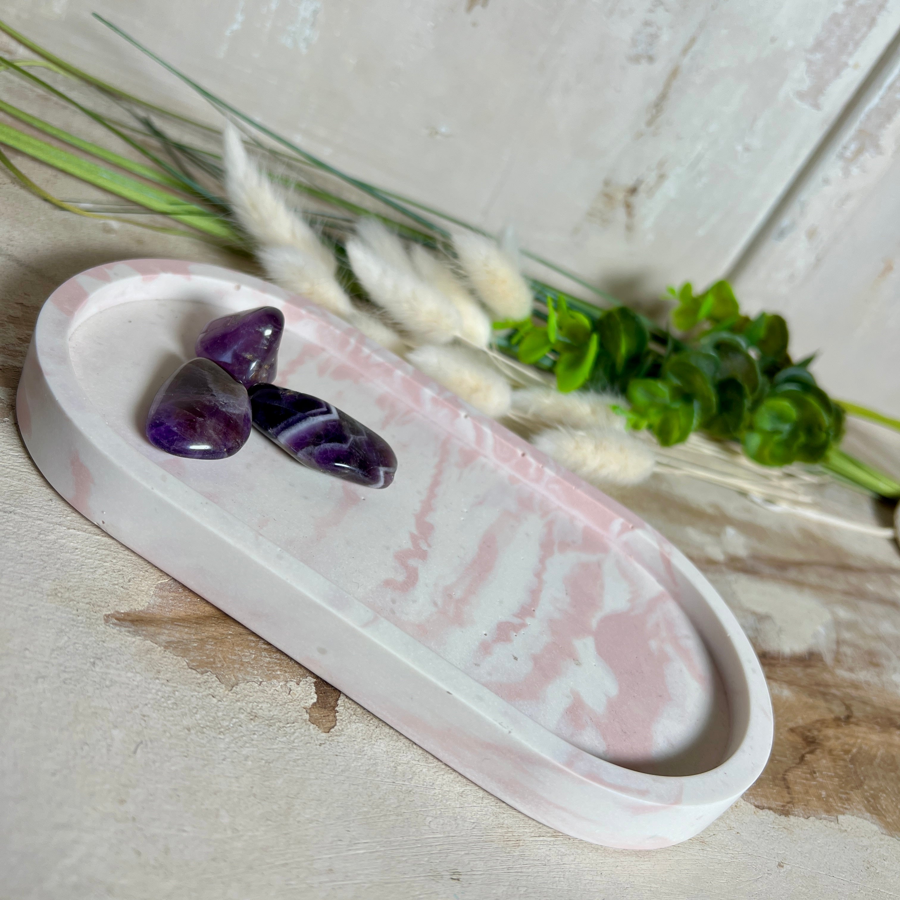 Schmucktablett aus Jesmonite in zartem Rosa-Weiß-Marmor. Handgegossenes, ovales Deko-Tablett mit glatter Oberfläche und Korkfüßen. Perfekt als Ablage für Schmuck, Schlüssel, Brille oder Dekoobjekte. Jedes Stück ein liebevoll gefertigtes Unikat in der Größe 17,5 × 9,5 × 1,7 cm.