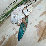 Unikat Anhänger aus stabilisiertem Holz mit türkisblauem Harzverlauf, schlanke Form, poliert. Verstellbares braunes Lederband 22–46 cm mit Schiebeknoten. Anhänger ca. 6,6 × 2 cm. Tragefoto am Hals und Produktfotos mit maritimer Deko