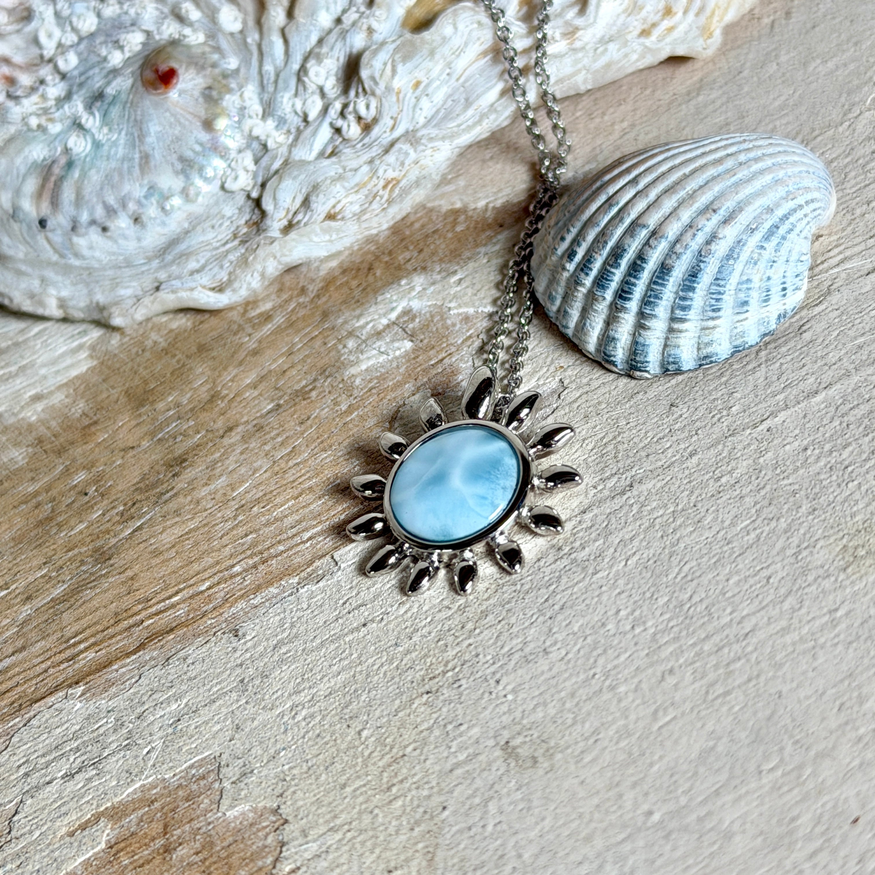 Feine Halskette aus rhodiniertem 925 Silber mit Sonnen-Anhänger und rundem Larimar-Cabochon, 10 mm. Der seltene, hellblaue Stein aus der Dominikanischen Republik erinnert an Meer und Himmel. Gesamtgröße des Anhängers ca. 20 x 19 mm, Ankerkette 45 cm, ca. 1 mm stark. Edler, maritimer Schmuck, geliefert in einer Geschenkbox.