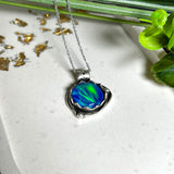 Handgemachter Anhänger mit rundem Cabochon aus Epoxidharz und schimmerndem synthetischem Opal. Die Farben changieren je nach Lichteinfall in Blau, Türkis und Grün. Der Opal sitzt in einer antik versilberten Fassung aus Messing (blei- & nickelfrei). Geliefert mit einer rhodinierten 925 Silberkette (45 cm). Jedes Stück ein Einzelstück – perfekt als stilvolles Geschenk oder persönlicher Glücksbringer.