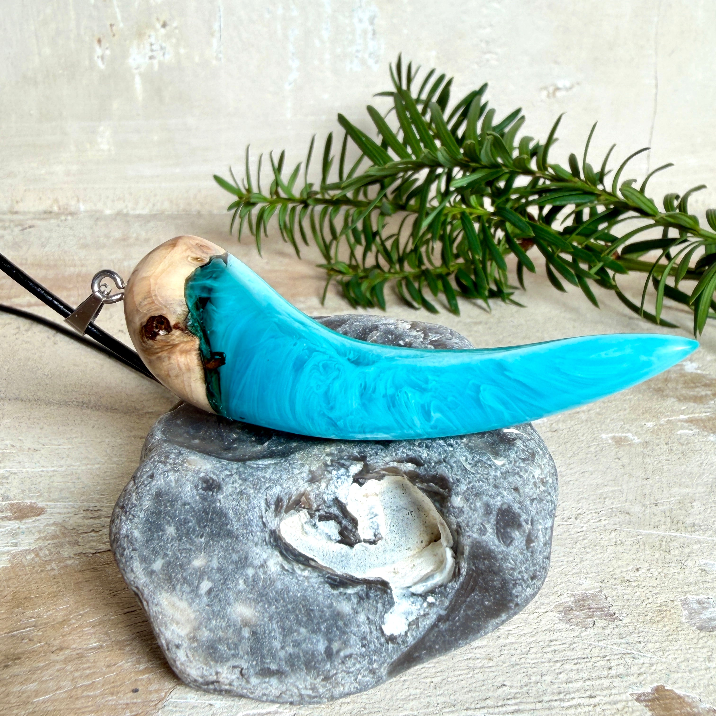 Handgefertigter Anhänger aus Edelholz und transparent-türkisblauem und weißen Epoxidharz, glatt poliert. Größe ca. 6,5 × 2,0 cm. Mit Edelstahlöse an schwarzer Lederkette (45 cm + 5 cm Edelstahl-Verlängerung, Karabiner). Moderner, unisex tragbarer Schmuck mit natürlicher Holzmaserung; kleine Lufteinschlüsse sind charakteristisch.