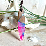 Handgefertigter Surfbrett-Anhänger aus Nussbaumholz und fluoreszierendem Epoxidharz in Pink, Blau und Weiß. Der Anhänger leuchtet zart bei Schwarzlicht und wird an einem verstellbaren Lederband (25–44 cm) mit Holzperlen getragen. Ein maritimes Unikat – ideal für Surfer und Naturliebhaber.