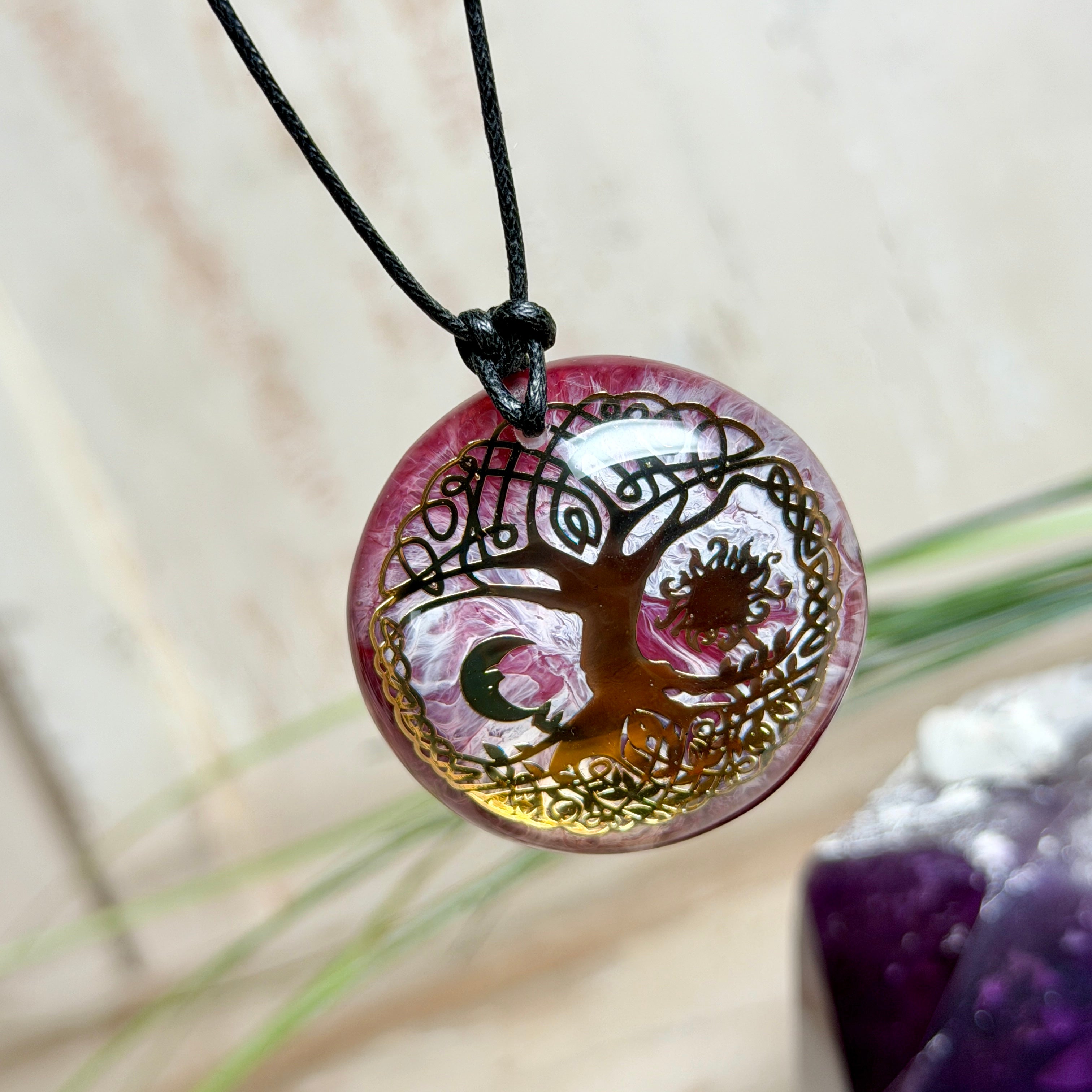 Detailfoto eines runden Yggdrasil Weltenbaum Anhängers (Baum des Lebens) aus Epoxidharz in lila, weiß und klar marmoriert. In der Mitte ein goldfarbenes Yggdrasil-Motiv aus Metall, eingefasst im klaren Harz. Durchmesser ca. 4 cm, getragen an einem verstellbaren gewachsten Baumwollband mit Schiebeknoten (Länge ca. 23–43 cm).