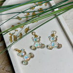 Kleiner Bärchen-Anhänger aus transparentem Harz mit irisierenden Flakes in Regenbogen-Schimmer, goldfarbene Anhängerschlaufe aus Edelstahl. Größe ca. 2,2 × 2,1 cm. Handgefertigtes Unikat; Flakes-Anordnung variiert, vereinzelt kleine Luftbläschen möglich.