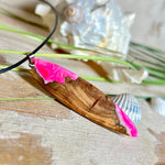 Handgefertigter Surfbrett-Anhänger „Pink Glow“ aus edlem Olivenholz und fluoreszierendem Epoxidharz in Pink & Weiß. Fluoreszierend bei Schwarzlicht, mit Edelstahl-Anhängerschlaufe und schwarzer Lederkette (45 cm + 5 cm Verlängerung). Ein maritimes Unikat – perfekt als Geschenk für Surfer und Meeresliebhaber.