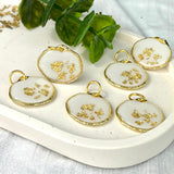Gold-colored pendant with gold flakes, background in white and fluorescent under black light, birthday, gift