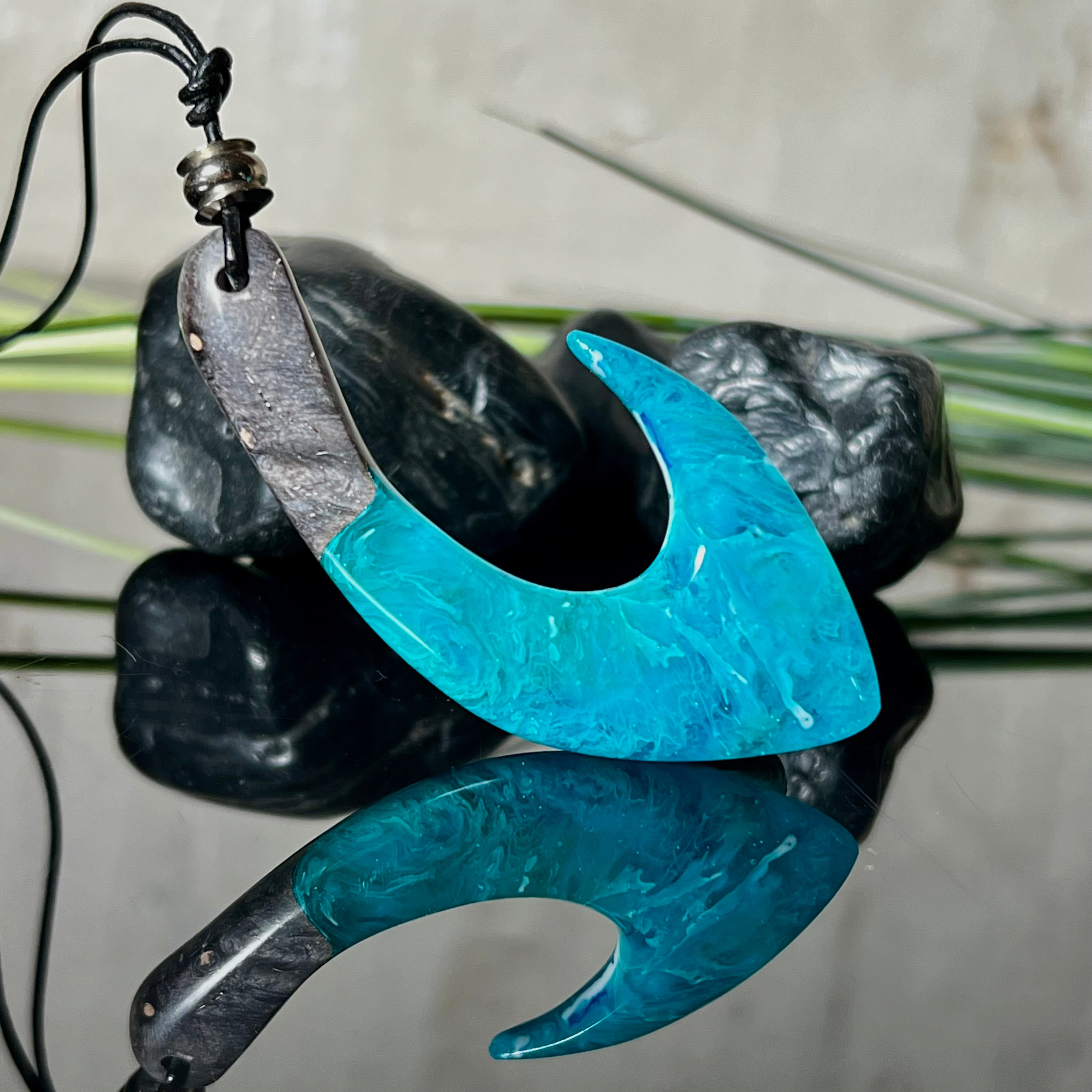 Handgefertigter Maori-Anhänger „Tangaroa Spirit“ in traditioneller Hakenform, gefertigt aus stabilisiertem Maserholz und ozeanblauem Harz. Die polierte Oberfläche bringt die natürlichen Maserungen und das tiefblaue Farbspiel besonders zur Geltung. Symbolisiert Schutz, Stärke und die Verbundenheit zum Meer. Verstellbares Lederband mit Schiebeknoten und dekorativen Holz- sowie Metallperlen – ideal als kraftvoller Talisman oder Geschenk.