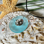 Handgefertigte Halskette mit Donut-Anhänger aus türkisfarbenem Seeglas, kombiniert mit einem filigranen Sonnen-Charm aus Edelstahl. Die Kette besteht aus einer schwarzen Lederschnur (1,5 mm) mit Karabiner und Verlängerungskette aus Edelstahl. Maritimes Schmuckstück für Meerliebhaberinnen und Sommerfreunde. Unikat mit stilvoller Ausstrahlung.