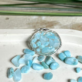 Runder Anhänger „Atlantis Dream“ aus antik-silberfarbener Zinklegierung, gefüllt mit kleinen Larimar-Edelsteinchen und klarem Resin. Die Larimarsteine zeigen sanfte Blau- und Weißtöne, die an das Meer erinnern. Durchmesser ca. 22 mm, handgefertigtes Unikat, fotografiert auf maritimem Untergrund mit kleinen Larimarsteinen und Muscheln zur Größenorientierung.