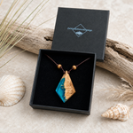 LAGUNENGLANZ Anhänger aus Goldfield-Maserholz und türkisem Epoxidharz in Rautenform, präsentiert in der Schmuckbox von ZeitlosSchmuckDesign – handgefertigter maritimer Naturschmuck am braunen Lederband mit Holzperlen, einzigartiges Unikat im edlen Küstenstil.