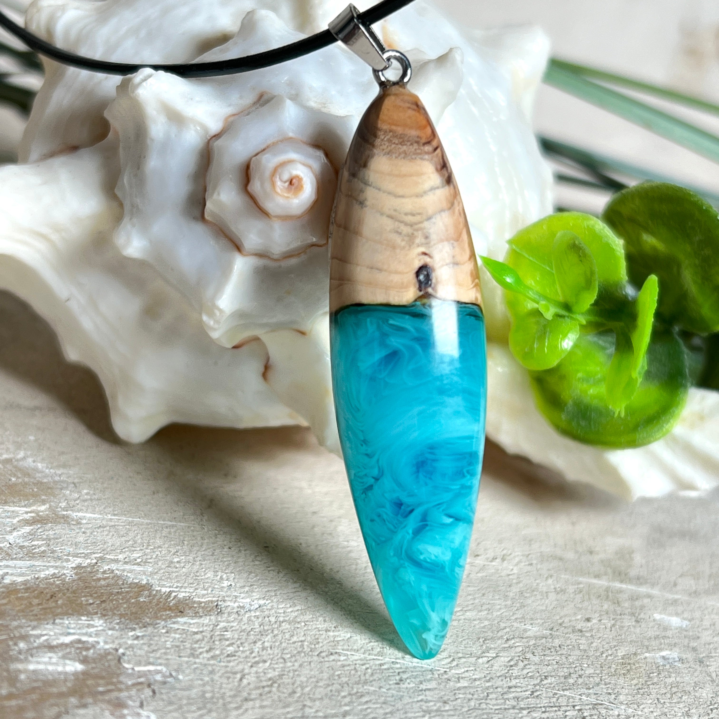 Anhänger aus Eibenholz und Epoxidharz in Blau-Türkis, Weiß und Transparent. Größe ca. 5,8 × 2 cm, Edelstahlöse, Lederkette 45+5 cm. Handgefertigtes Unikat inspiriert vom Ozean.