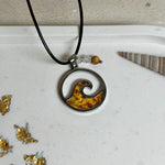 “Runder Wellenanhänger aus Edelstahl mit Bernstein-Harz-Inlay, Jaspisperle & facettiertem Bergkristall an schwarzer Lederkette (45 cm + 5 cm).”