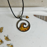 “Runder Wellenanhänger aus Edelstahl mit Bernstein-Harz-Inlay, Jaspisperle & facettiertem Bergkristall an schwarzer Lederkette (45 cm + 5 cm).”