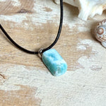 Larimar Freeform Anhänger an schwarzer Lederkette. Natürlicher, rechteckiger Larimar-Stein (ca. 1,5 × 1 cm) in Türkis-Blau mit weißen Strukturen, eingefasst in eine rhodinierte Silberöse. Beidseitig tragbar, an 45 cm Lederkette mit Edelstahl-Karabinerverschluss und 5 cm Verlängerung. Maritimes, zurückhaltend elegantes Schmuckstück mit der Optik karibischen Meerwassers.