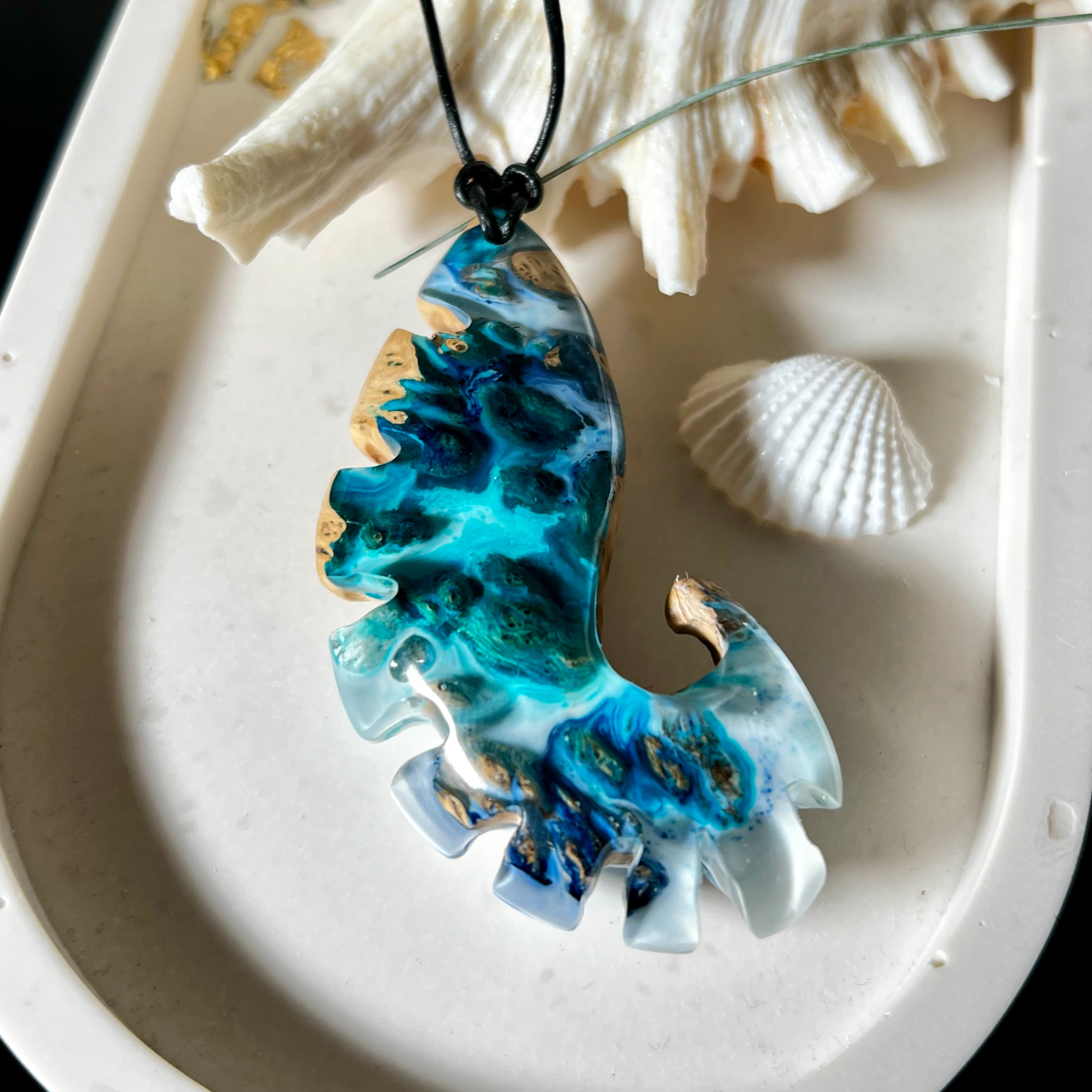 Ocean Nautilus Halskette – handgefertigter Anhänger aus  Epoxidharz und edlem Maserholz in kräftigem Blau, Türkis und Weiß, geformt wie eine stilisierte Nautilus-Muschel. Die einzigartige Maserung des Holzes trifft auf transparente Tiefenwirkung des Harzes. Der ca. 7 cm große Anhänger hängt an einem verstellbaren Lederband mit dekorativen Holzperlen (26–48 cm). Jedes Stück ist ein maritimes Unikat, inspiriert von der Magie des Meeres.