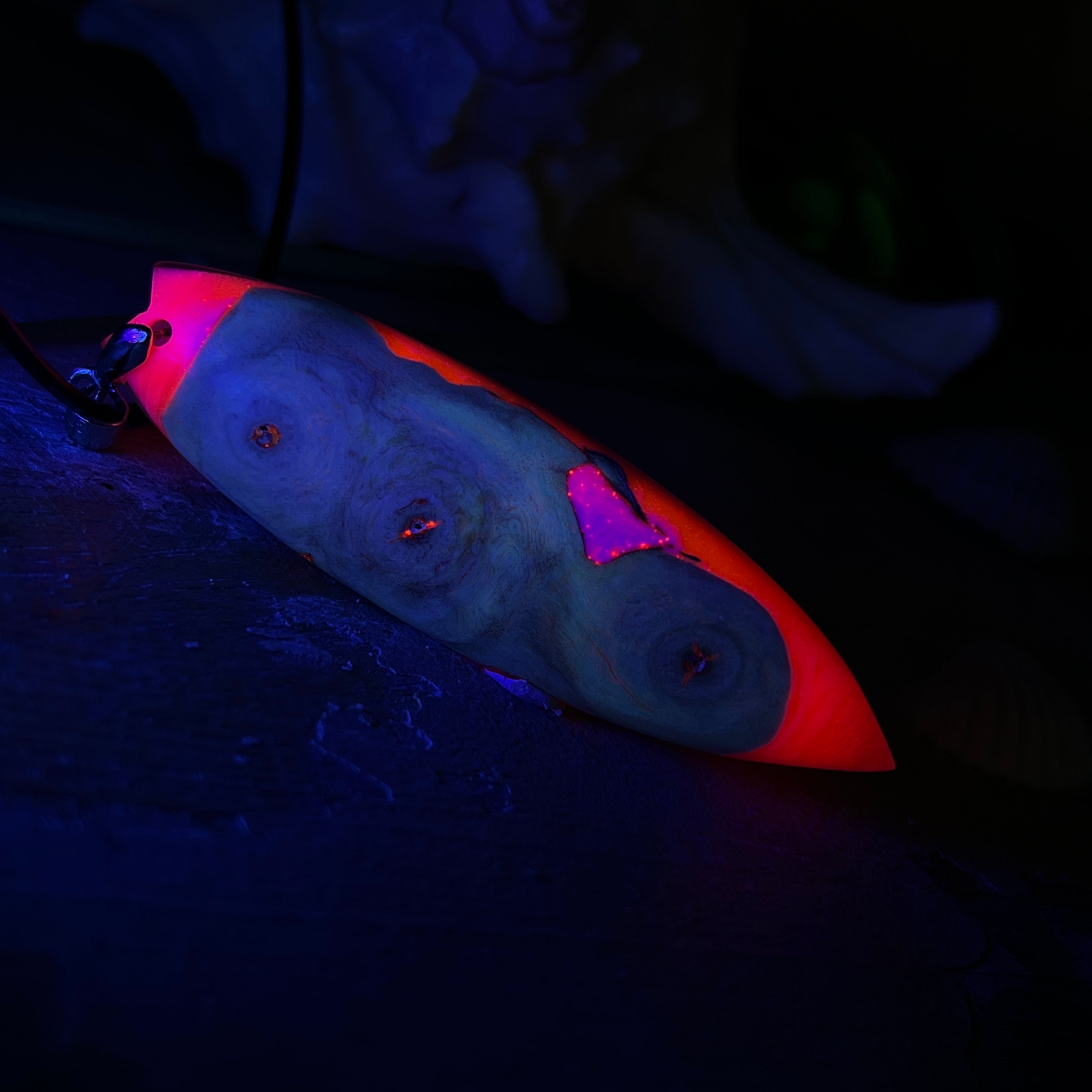 Handgefertigter Surfbrett-Anhänger „Flame Surf“ aus Maserholz und fluoreszierendem Harz in kräftigem Pink. Das Schmuckstück leuchtet bei Schwarzlicht und wird an einer schwarzen Lederkette mit Edelstahl-Karabiner (45 cm + 5 cm Verlängerung) geliefert. Größe ca. 6,7 × 2 cm. Ein Unikat für Surf- und Strandliebhaber, edel verarbeitet und mit Liebe gefertigt.