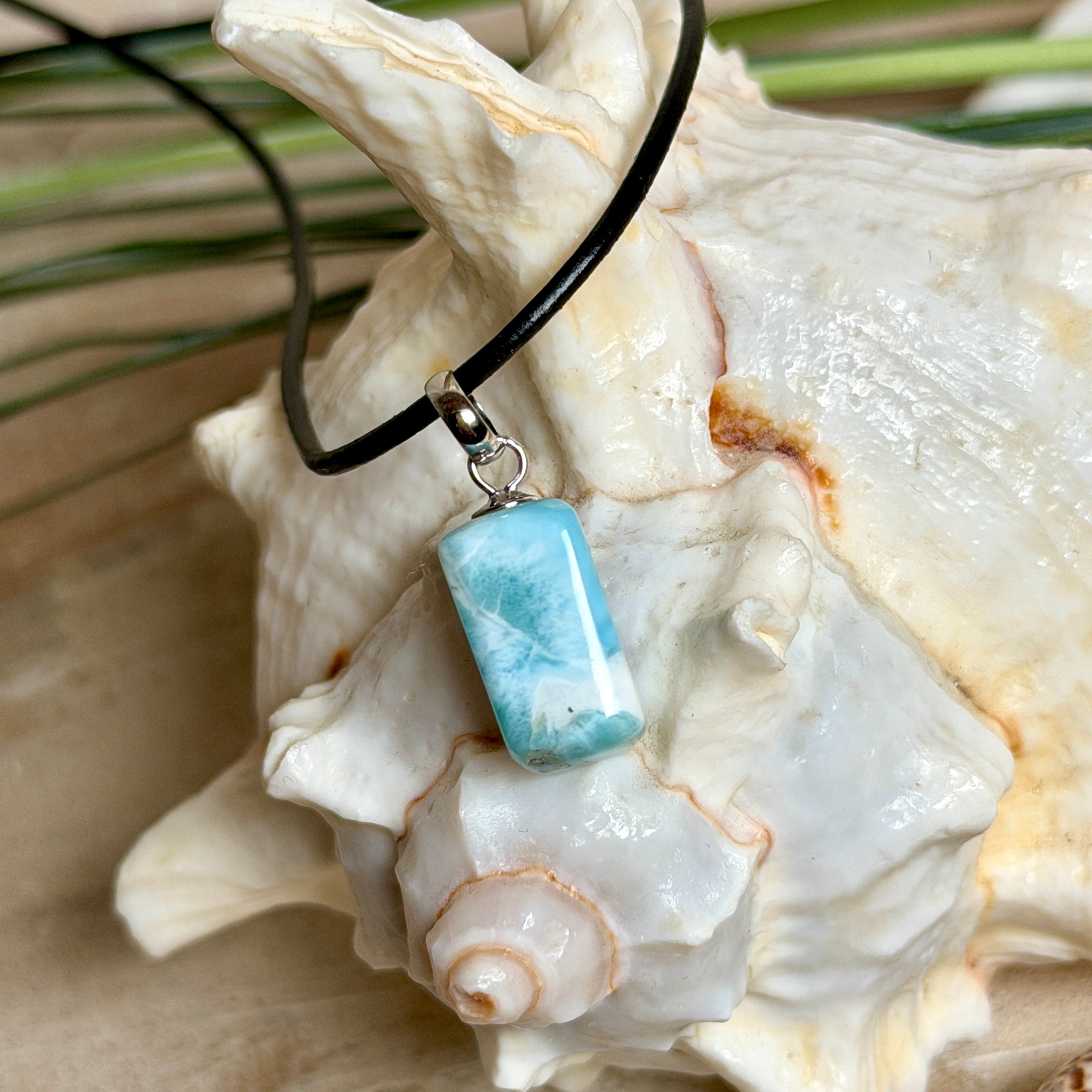 Larimar Freeform Anhänger an schwarzer Lederkette. Natürlicher, rechteckiger Larimar-Stein (ca. 1,5 × 1 cm) in Türkis-Blau mit weißen Strukturen, eingefasst in eine rhodinierte Silberöse. Beidseitig tragbar, an 45 cm Lederkette mit Edelstahl-Karabinerverschluss und 5 cm Verlängerung. Maritimes, zurückhaltend elegantes Schmuckstück mit der Optik karibischen Meerwassers.