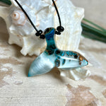 Handgefertigter Walflossen-Anhänger „Flossenklang“ aus Maserholz und türkis-blau-grau-weiß marmoriertem Epoxidharz an verstellbarem Lederband. Maritime Kette als Unikatschmuck für Meeresliebhaber und Wal-Fans, hochwertig poliert, präsentiert vor Muscheldeko und in Schmuckbox von ZeitlosSchmuckDesign.