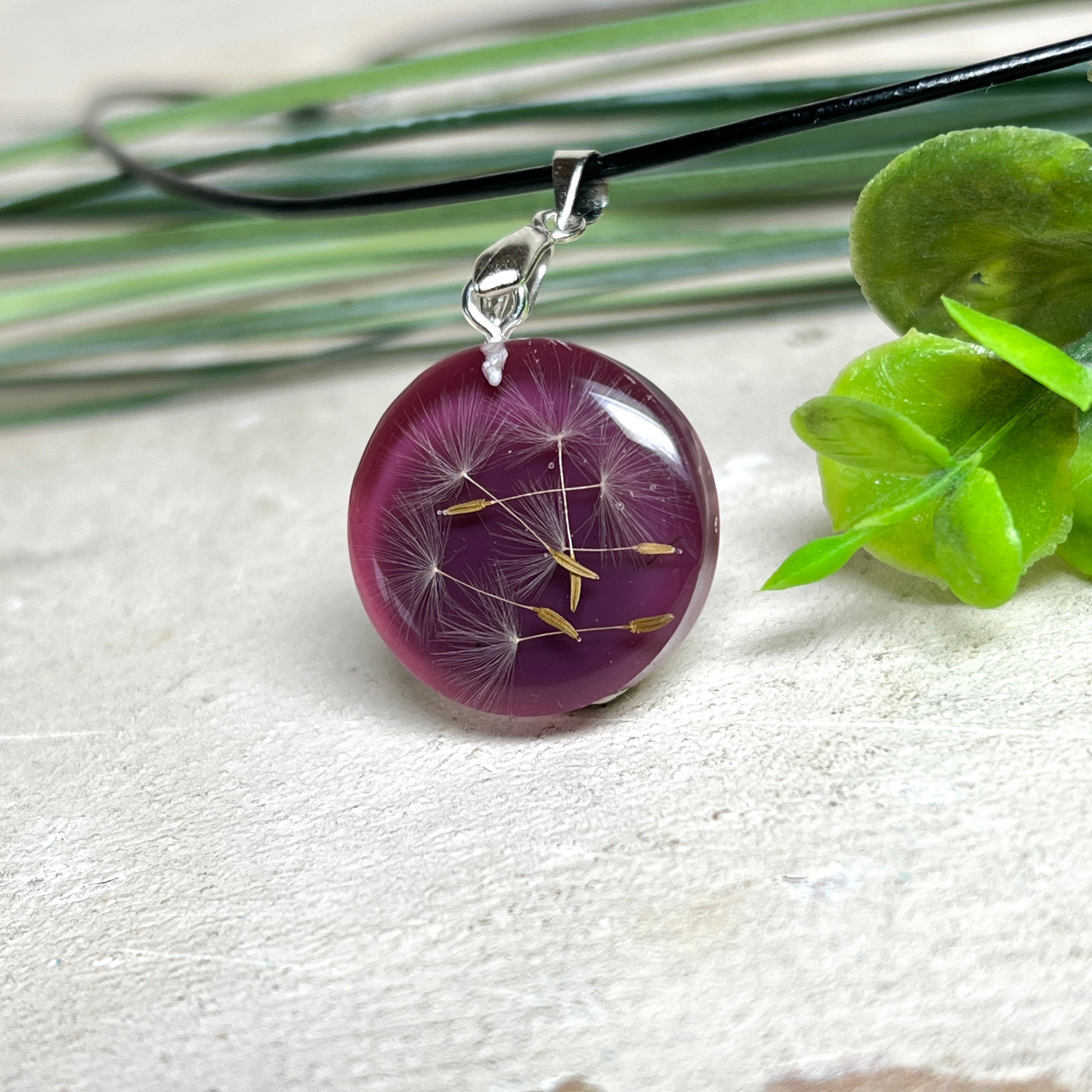 Runder Pusteblumen-Anhänger aus Harz, Hintergrund Brombeerfarben. Durchmesser 22 mm, Edelstahlöse, Lederkette verstellbar mit Edelstahlverschluss.