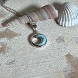 Feine Wellen-Kette aus rhodiniertem 925 Silber. Der runde Anhänger zeigt eine stilisierte Welle mit hellblauem Larimar-Cabochon, eingefasst in poliertem Silber. Größe des Anhängers ca. 23 x 13 mm, an einer 45 cm langen, 1 mm starken, rhodinierten Silberkette. 
