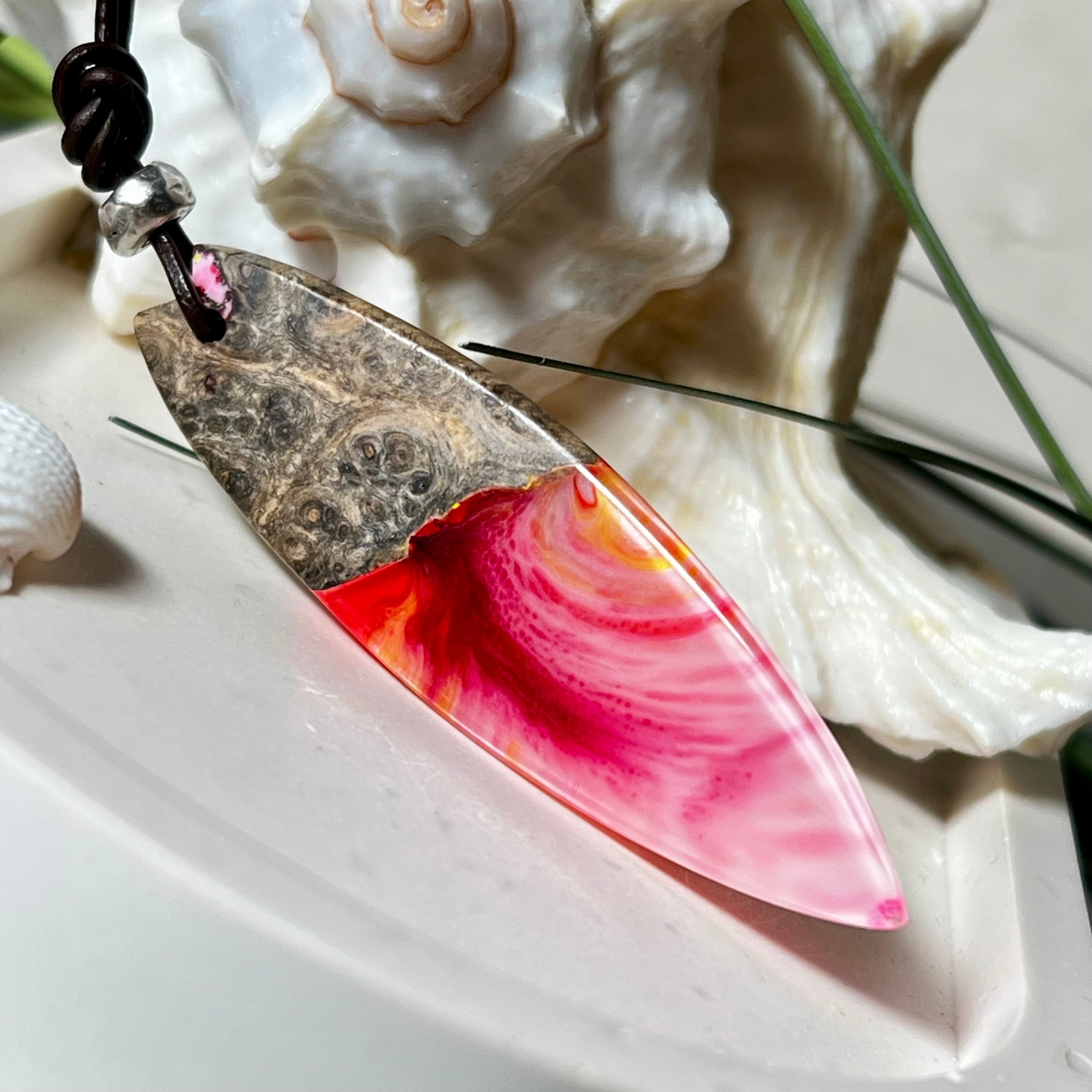 Aurora Flame – fluoreszierender Surfbrett-Anhänger aus Maserholz und leuchtendem Epoxidharz in Rosa, Pink, Orange und Weiß. Der handgefertigte Unikat-Anhänger fluoresziert bei Schwarzlicht in intensiven Farbtönen. Er ist ca. 6,3 x 2 cm groß, wird an einem verstellbaren Lederband (26–45 cm) getragen und ist mit einer silberfarbenen Spacerperle verziert. Ein ausdrucksstarkes Schmuckstück für Menschen mit Persönlichkeit.