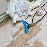 Handgefertigter Walflossen-Anhänger aus Olivenholz und Epoxidharz in Blau-Grün-Weiß, polierte Oberfläche, Edelstahl-Öse. Schwarze Lederkette 45 cm mit Edelstahl-Karabinerverschluss und 5 cm Edelstahl-Verlängerung. Anhängergröße ca. 2,5 × 3,2 cm, maritime Produktfotografie.