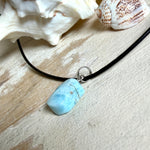 Larimar Freeform Anhänger mit rhodinierter Silberöse an schwarzer Lederkette. Der seltene, kostbare Larimar („Atlantisstein“) zeigt ein lebendiges Muster aus Türkis- und Weißtönen. Beidseitig tragbar, Steingröße ca. 2 x 1 cm, Lederkette 45 cm mit Edelstahl-Karabiner und 5 cm Verlängerung. Natürlicher, maritimer Unikatschmuck.