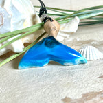 Handgefertigter Walflossen-Anhänger aus Olivenholz und glänzendem Harz in Blau-Grün-Weiß – maritimer Schmuck „Flossenklang“. Der Anhänger erinnert an die Form einer Walflosse und vereint die natürliche Maserung des Holzes mit dem schimmernden Farbspiel des Harzes. Mit verstellbarem schwarzen Lederband und Spacerperle. Ideal für Meeresliebhaber und Naturliebhaber – jedes Stück ein Unikat.