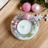 Runder Teelichthalter aus klarem Epoxidharz, Durchmesser ca. 7 cm, Höhe ca. 4 cm. Im Harz sind rosa Weihnachtskugeln, ein Stern, eine Schneeflocke, ein Tannenbaum, künstliche Tannennadeln und feiner Glitzer eingegossen. Vertiefung für ein Teelicht in der Mitte, Unterseite mit vier Korkpads als Möbelschoner. Fotografiert auf Holz mit Tannenzweig und rosa Kugeln als weihnachtliche Dekoration